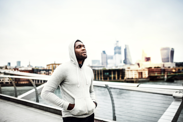 Black man runner walking on the bridge in a city, hood on head. Copy space.