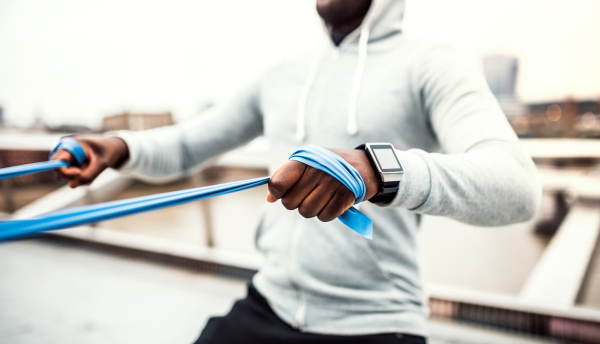 Unrecognizable young active black sportsman exercising with elastic rubber bands on the bridge in London.