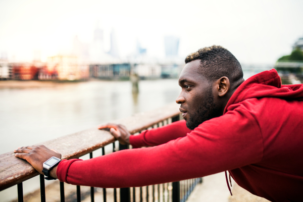 Young sporty black man runner stretching on the bridge outside in a city.