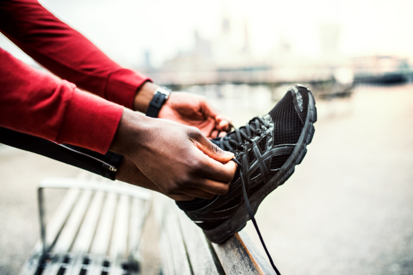 A close-up of an unrecognizable young sporty black man runner tying shoelaces before running outside in a city.