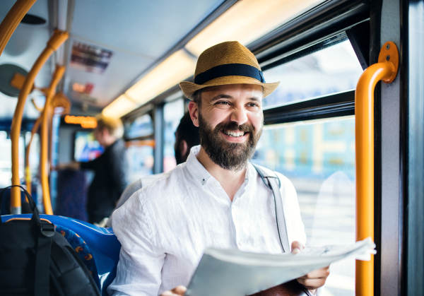 Hipster man sitting on a bus in the city, travelling to work and reading newspapers.