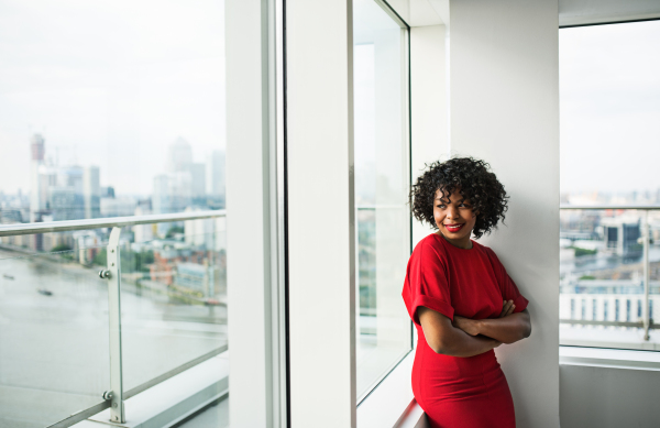 A portrait of woman standing by the window against London rooftop view panorama. Copy space.