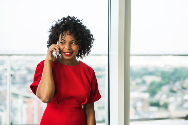 A portrait of woman with smartphone standing by the window, making a phone call. Copy space.