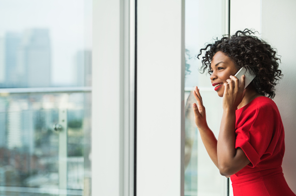 A portrait of woman with smartphone standing by the window, making a phone call. Copy space.