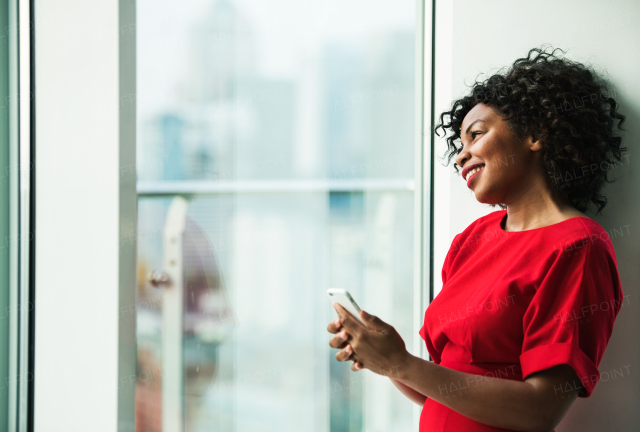 A portrait of happy woman standing by the window, holding smartphone. Copy space.