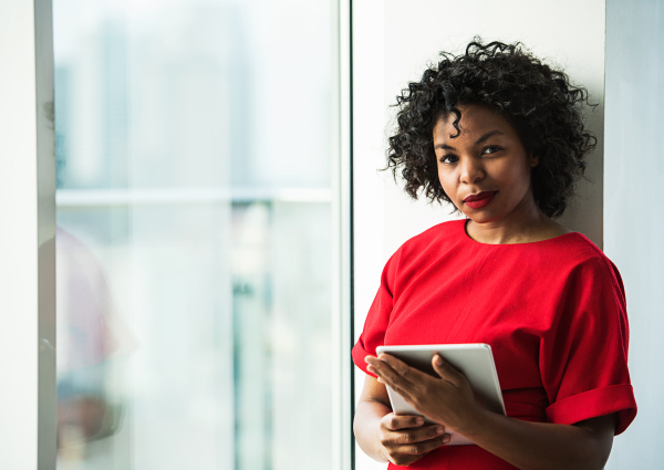 A portrait of woman with tablet standing by the window against London panorama. Copy space.