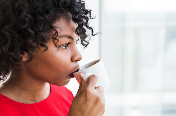 A close-up of a woman standing by the window drinking coffee. Copy space.