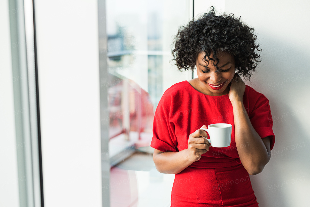 A close-up of a woman standing by the window holding coffee cup, looking down. Copy space.