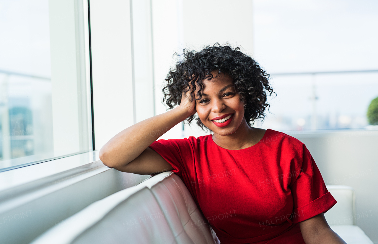 A portrait of happy black woman sitting on a sofa by the window in an office.