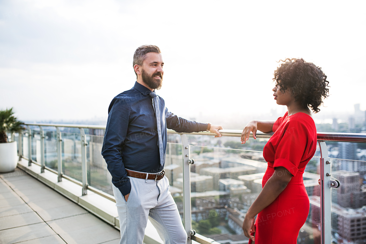 A portrait of businesspeople standing against London rooftop view, leaning on a railing and talking.