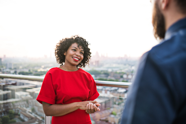 Two businesspeople standing against London rooftop view panorama, talking.