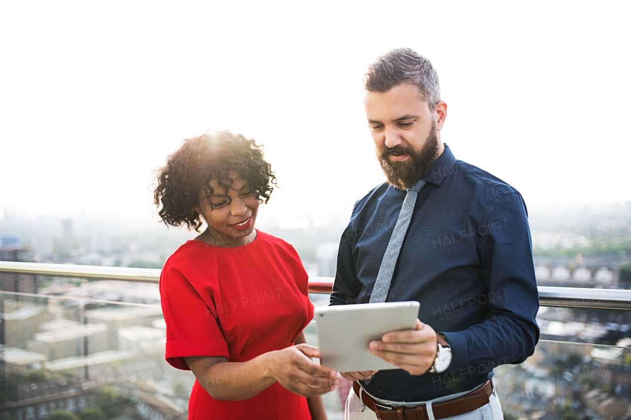 A portrait of businesspeople with tablet standing against London rooftop view, discussing issues.