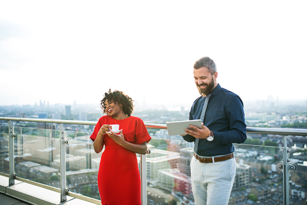 A portrait of businesspeople with tablet and coffee standing against London rooftop view, discussing issues.