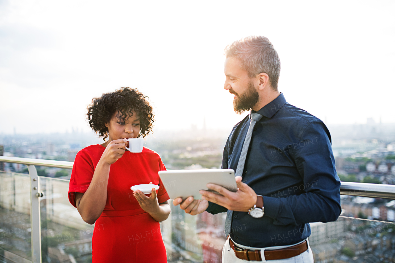 A portrait of businesspeople with tablet and coffee standing against London rooftop view, discussing issues.