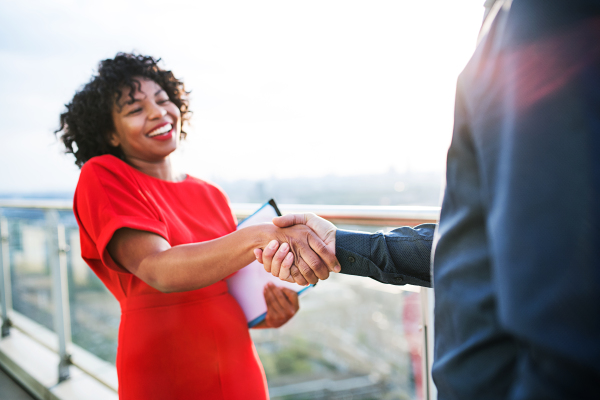 Two young businesspeople standing on a terrace in London, shaking hands.