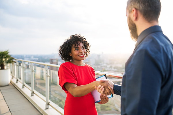 A portrait of businesspeople standing against London rooftop view, shaking hands.