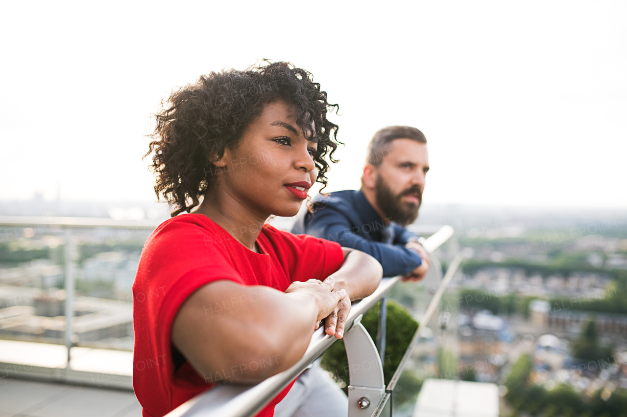 A portrait of businesspeople standing against London rooftop view, leaning on a railing.