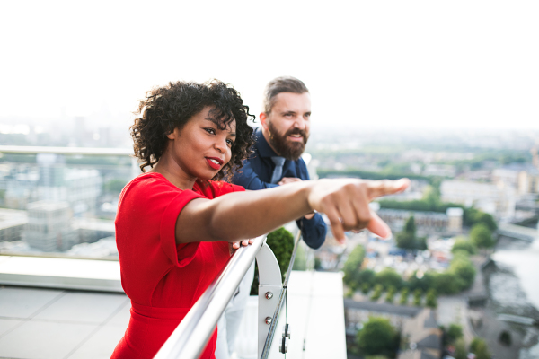 A portrait of businesspeople standing against London rooftop view, pointing to something and talking.