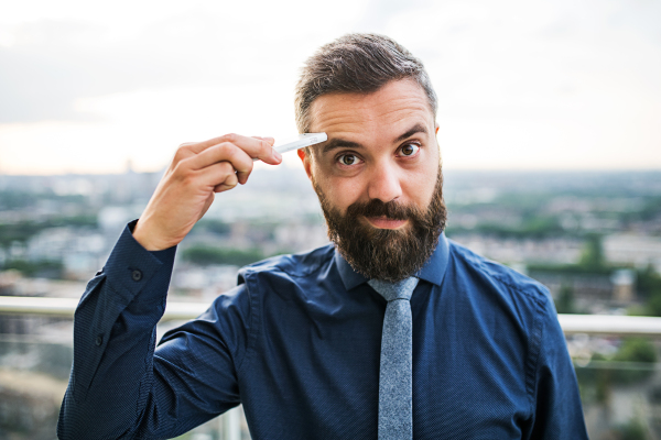 A close-up portrait of businessman with smartphone standing against London rooftop view panorama.