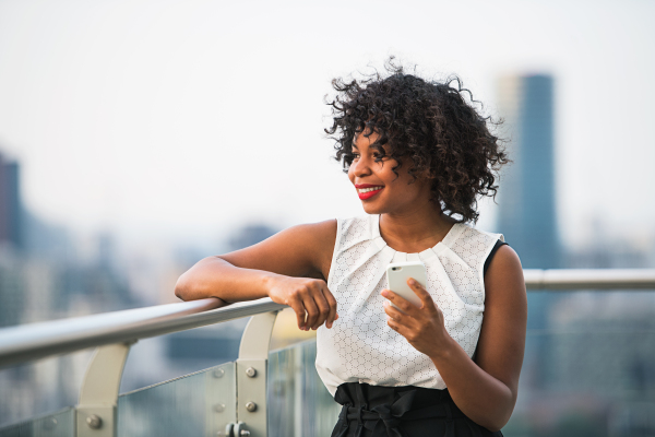 A businesswoman with smartphone standing against London view panorama, text messaging.