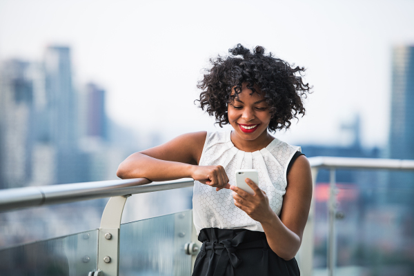 A portrait of black businesswoman standing against London rooftop view panorama, text messaging. Copy space.