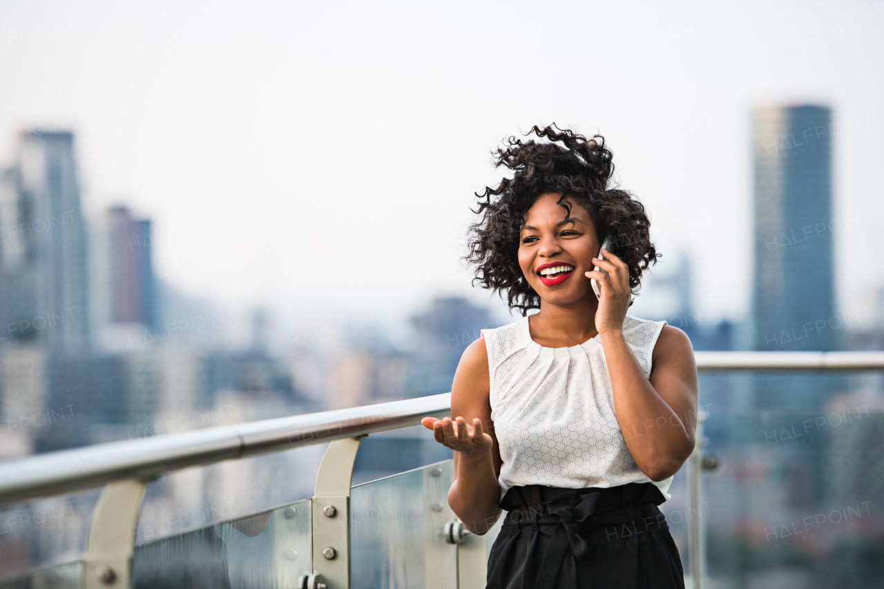 A portrait of black businesswoman standing against London rooftop view panorama, making a phone call. Copy space.