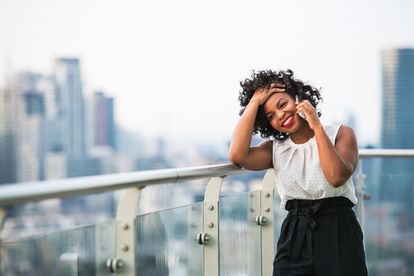 A portrait of black businesswoman standing against London rooftop view panorama, making a phone call. Copy space.