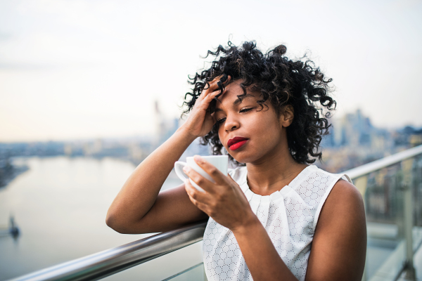 A close-up portrait of a black woman standing on a terrace, drinking coffee. Copy space.