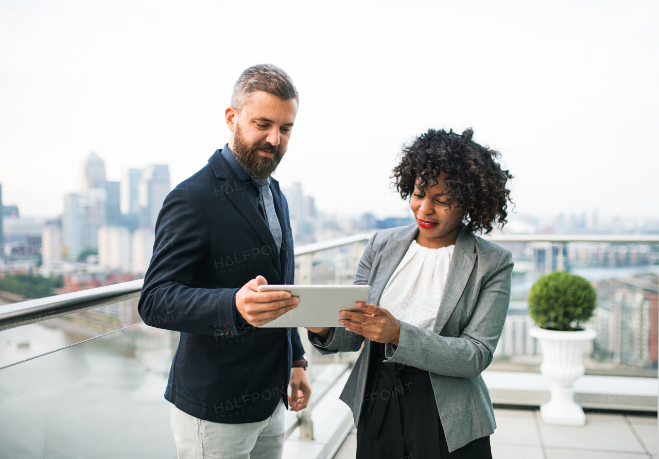 A portrait of businesspeople with tablet standing against London rooftop view, discussing issues.