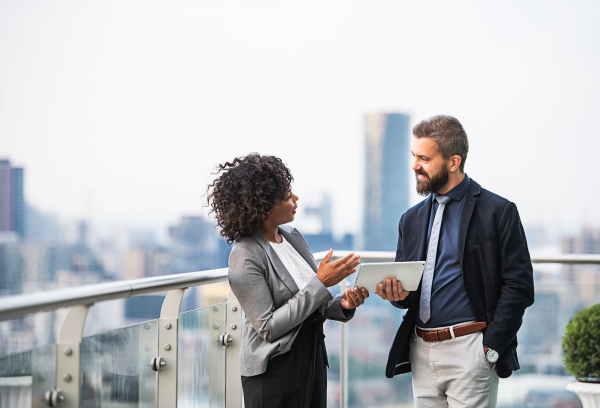 A portrait of businesspeople with tablet standing against London rooftop view, discussing issues.