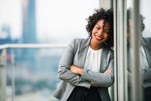 A portrait of black businesswoman standing on a terrace against London rooftop view panorama, arms crossed. Copy space.