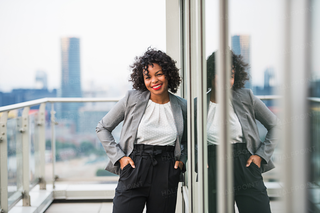 A portrait of black businesswoman standing on a terrace in London, hands in pockets. Copy space.