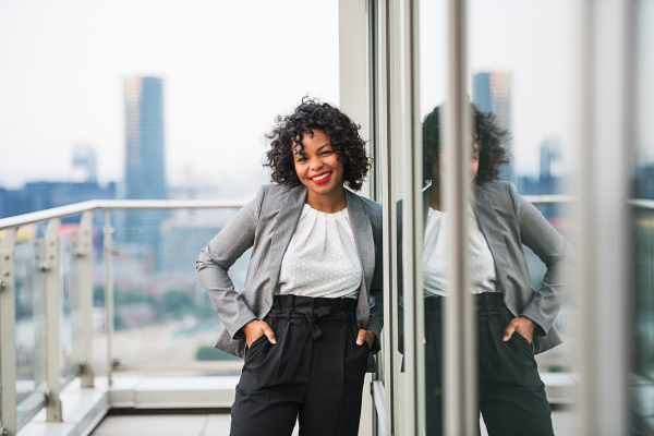 A portrait of black businesswoman standing on a terrace in London, hands in pockets. Copy space.