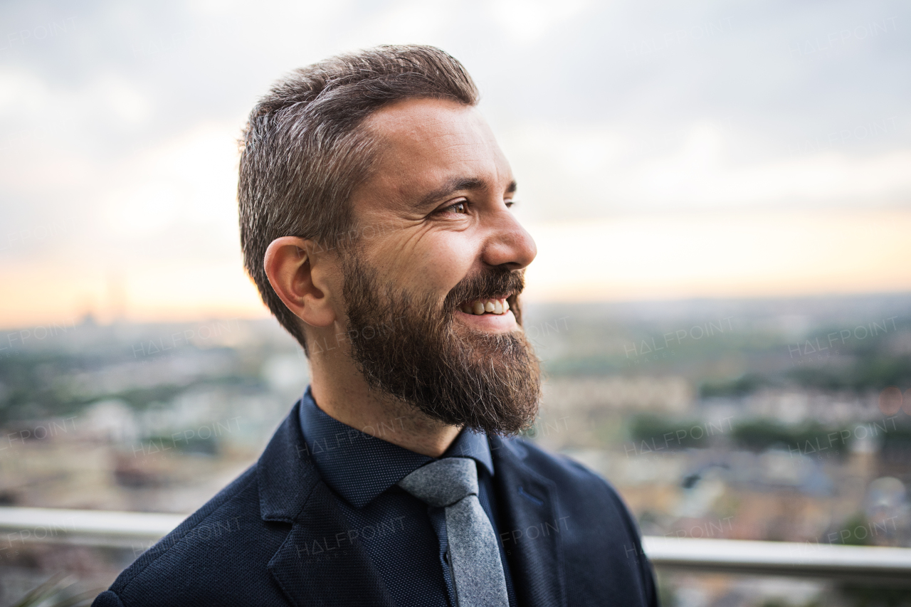 A portrait of businessman standing against London rooftop view panorama at sunset. Close-up.