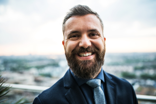 A portrait of businessman standing against London rooftop view panorama at sunset. Close-up.