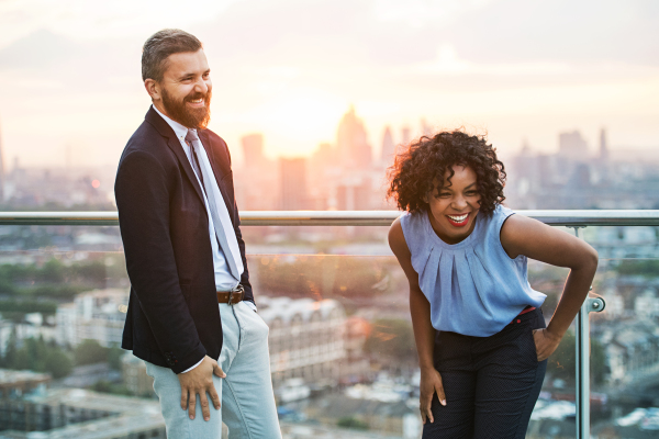 A portrait of businesspeople standing against London rooftop view at sunset, laughing.