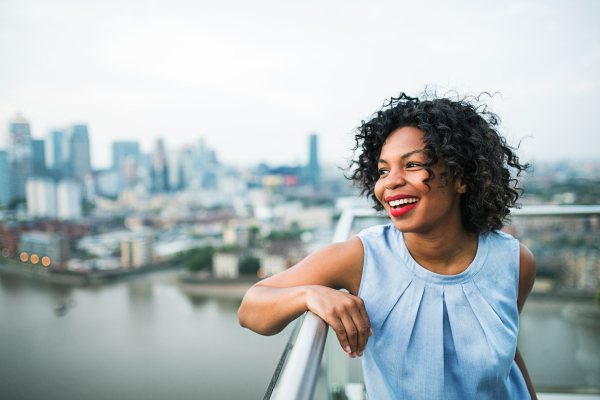 A portrait of a laughing black woman standing on a terrace in London. Copy space.