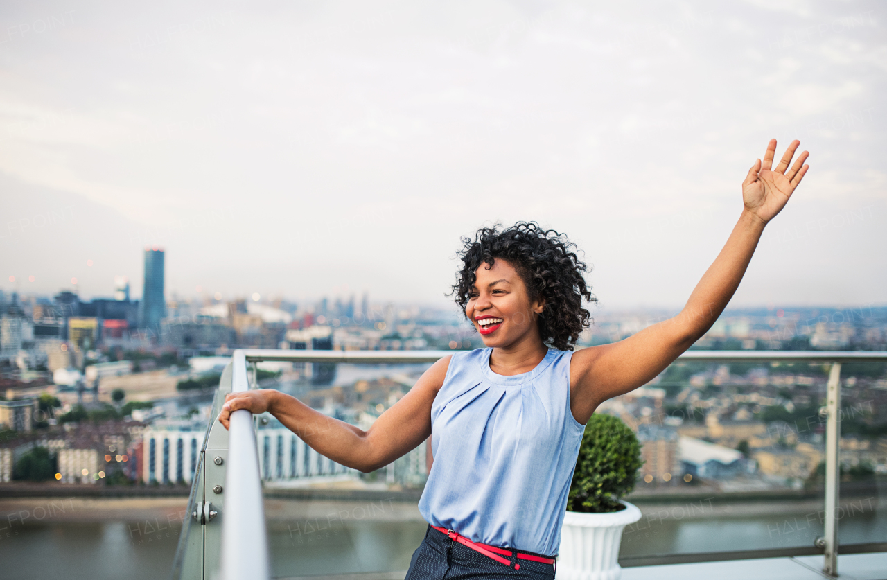 A portrait of cheerful black businesswoman standing against London rooftop view panorama. Copy space.