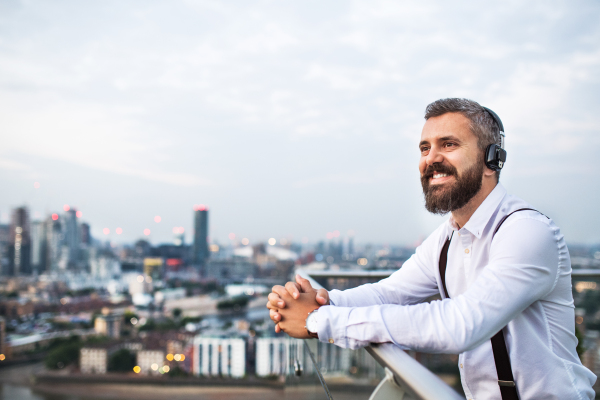 A businessman with headphones standing against London view panorama, listening to music. Copy space.