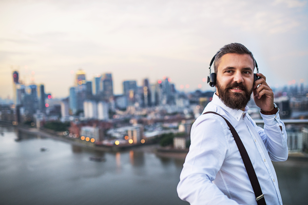 A businessman with headphones standing against London view panorama, listening to music. Copy space.