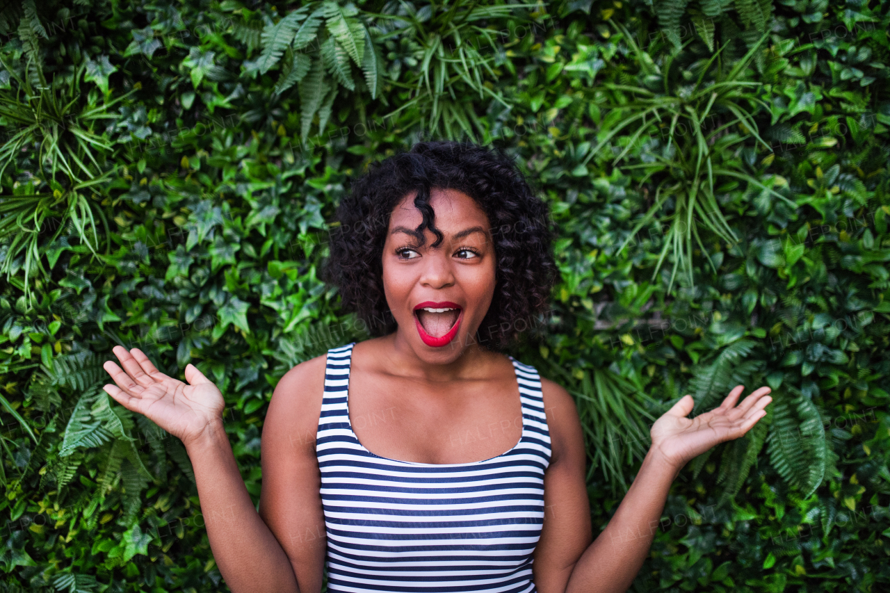 A portrait of a black laughing woman standing against green background of bush leaves.