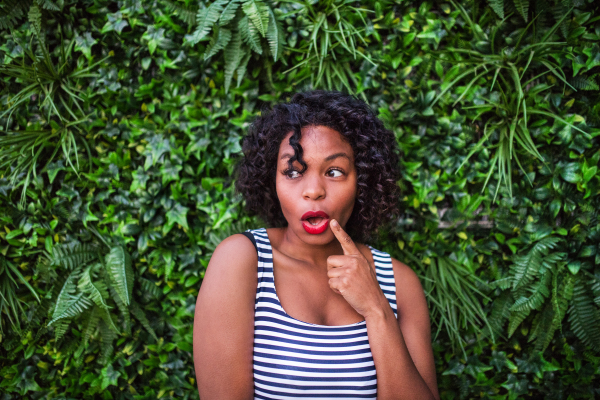 A portrait of a suprised woman standing against green background of bush leaves.