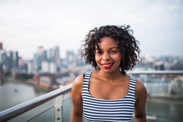 A portrait of black businesswoman standing against London rooftop view panorama. Copy space.