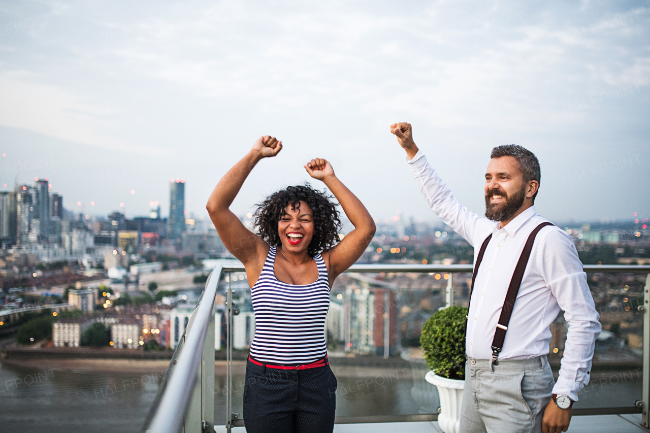 A portrait of businesspeople standing against London rooftop view panorama at sunset, laughing and expressing excitement.