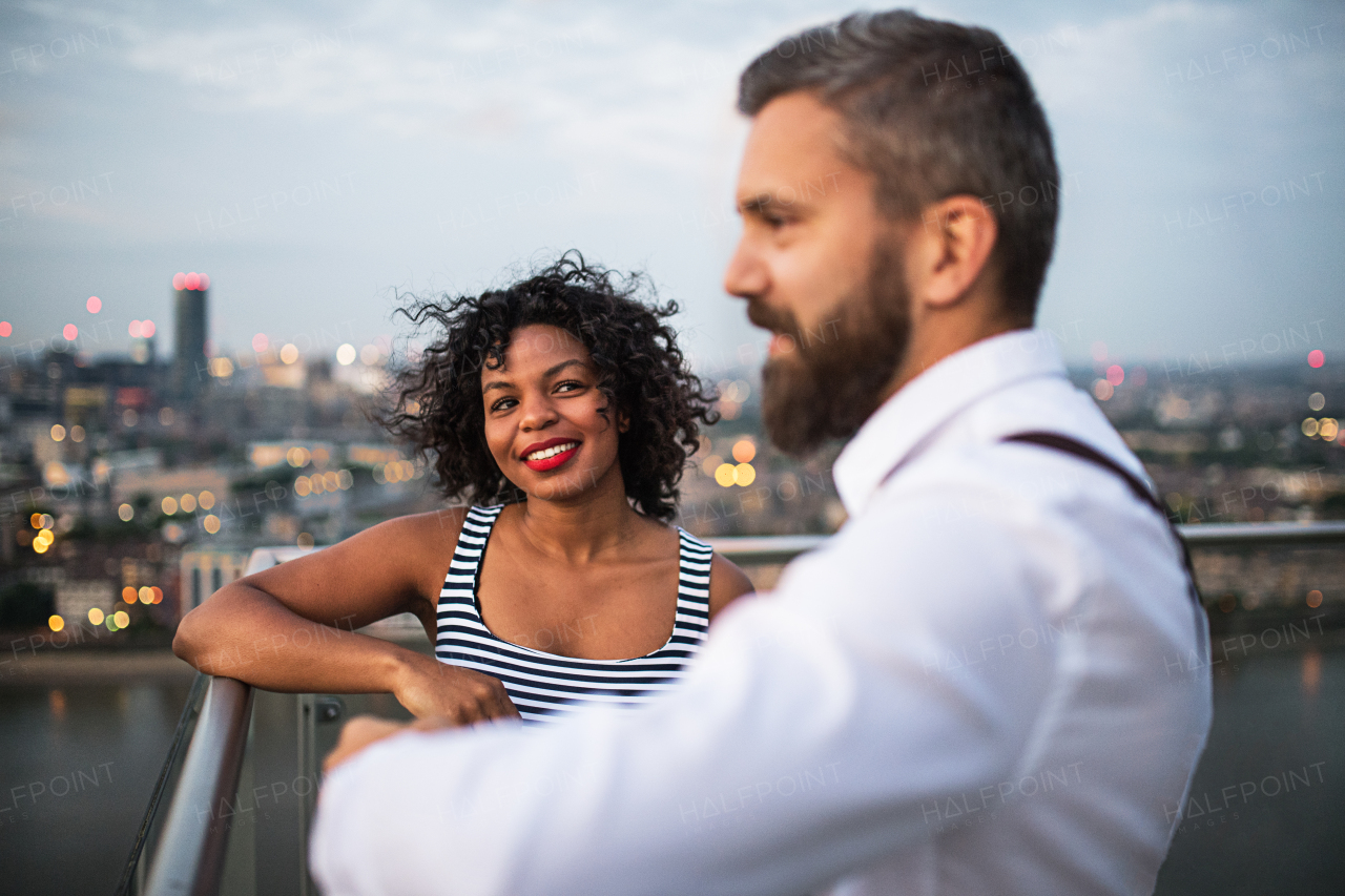 A portrait of businesspeople standing against London rooftop view panorama at sunset, talking.