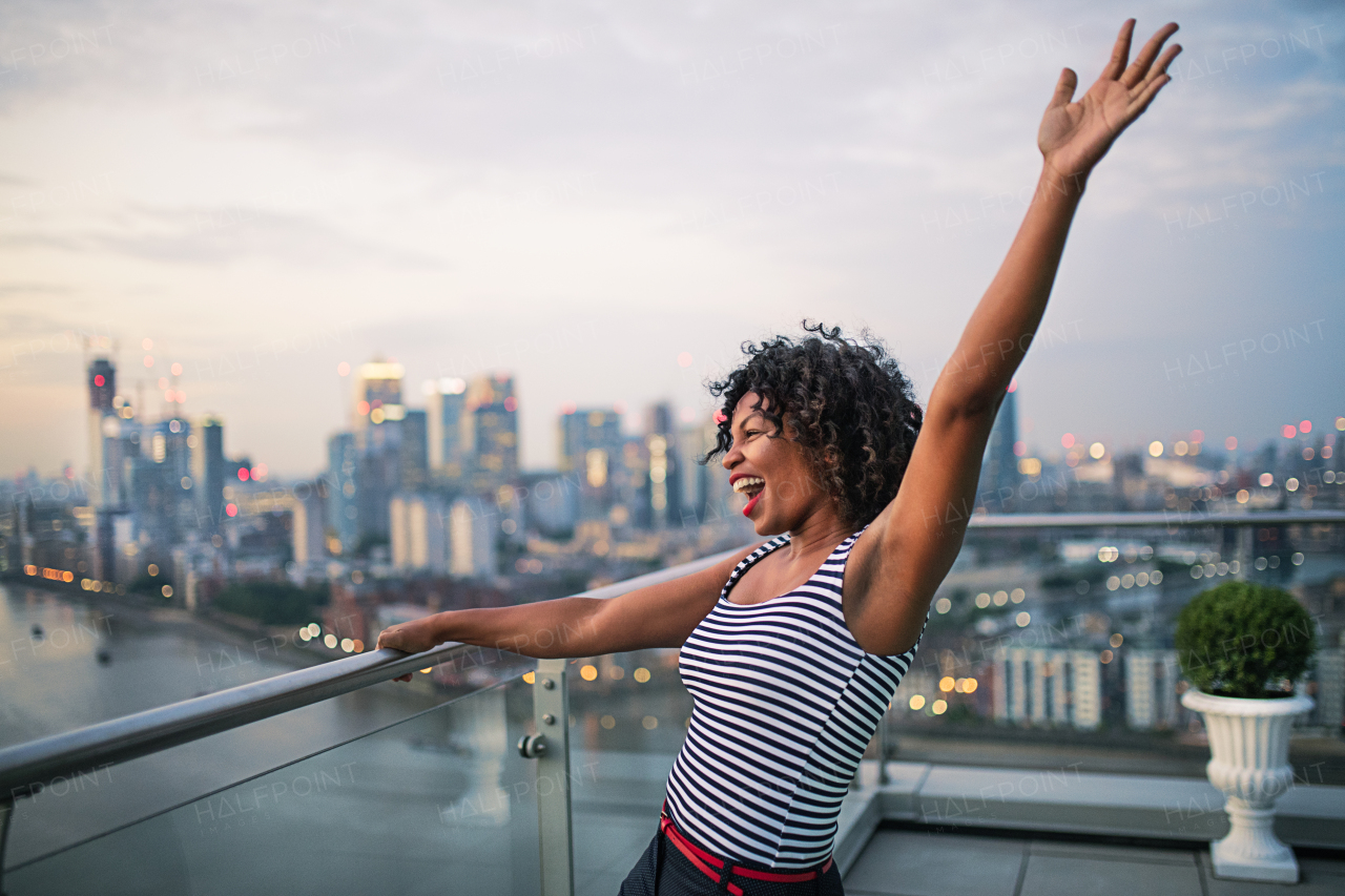 A portrait of black businesswoman standing against London rooftop view panorama, expressing excitement. Copy space.