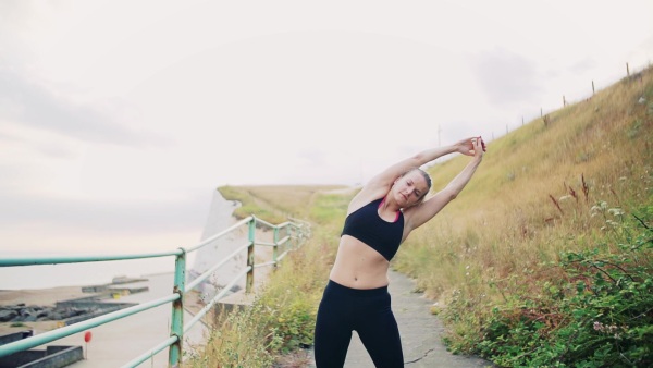 Young sporty woman runner stretching outside on the beach in nature. Slow motion.