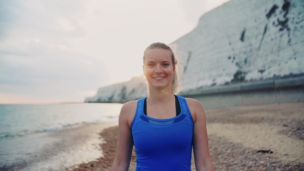 Young sporty woman runner in blue sportswear walking outside on the beach in nature. Copy space. Slow motion.