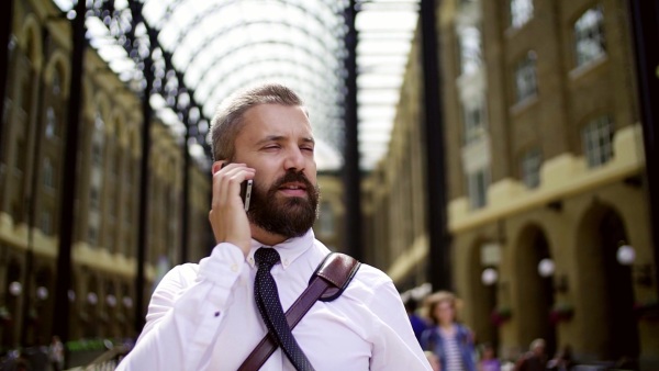 Happy businessman with smartphone on the trian station in London, making a phone call. Slow motion.