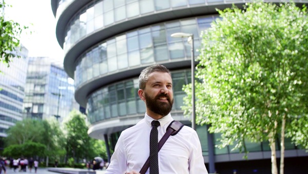 A portrait of hipster businessman with laptop bag standing on the street in London. Slow motion.